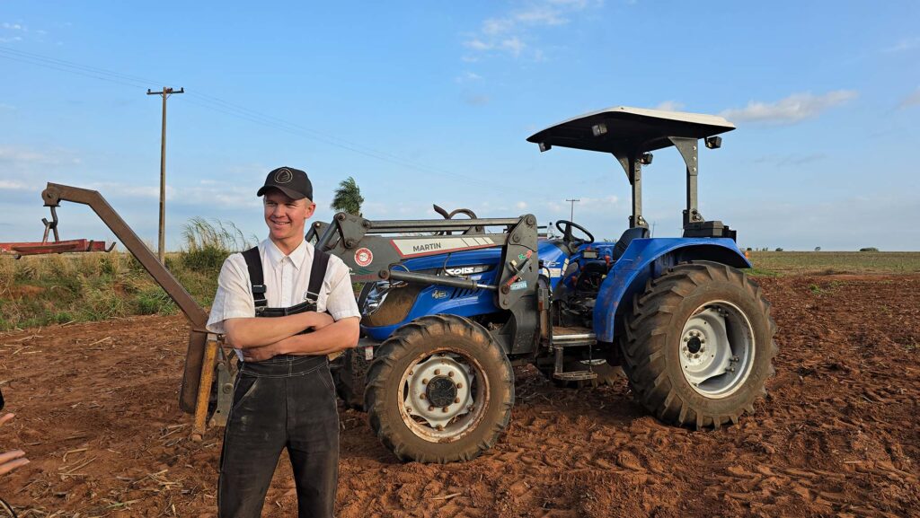 Jovem menonita de macacão tradicional em frente a um trator na colônia Nueva Durango, Paraguai.