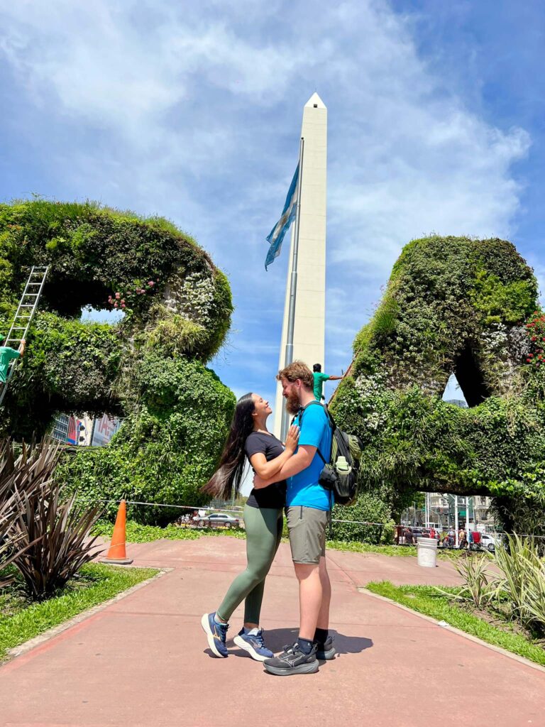 Mari e Arthur do Fomos Viajar em frente ao Obelisco na Avenida 9 de Julio, Buenos Aires.