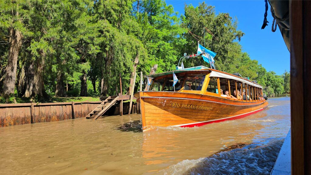 Barco de passeio navegando pelo Delta do Rio Paraná em Tigre, Argentina, com vegetação típica ao fundo.