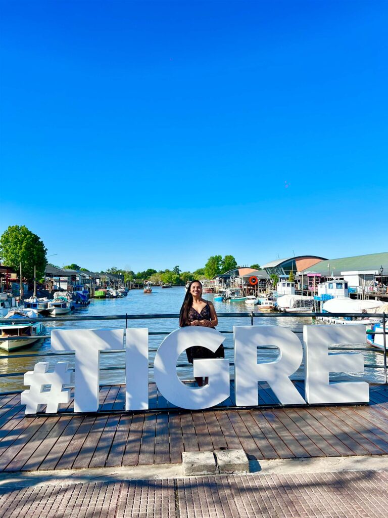 Letreiro turístico com o nome da cidade de Tigre, Argentina, com a Mari posando ao lado.